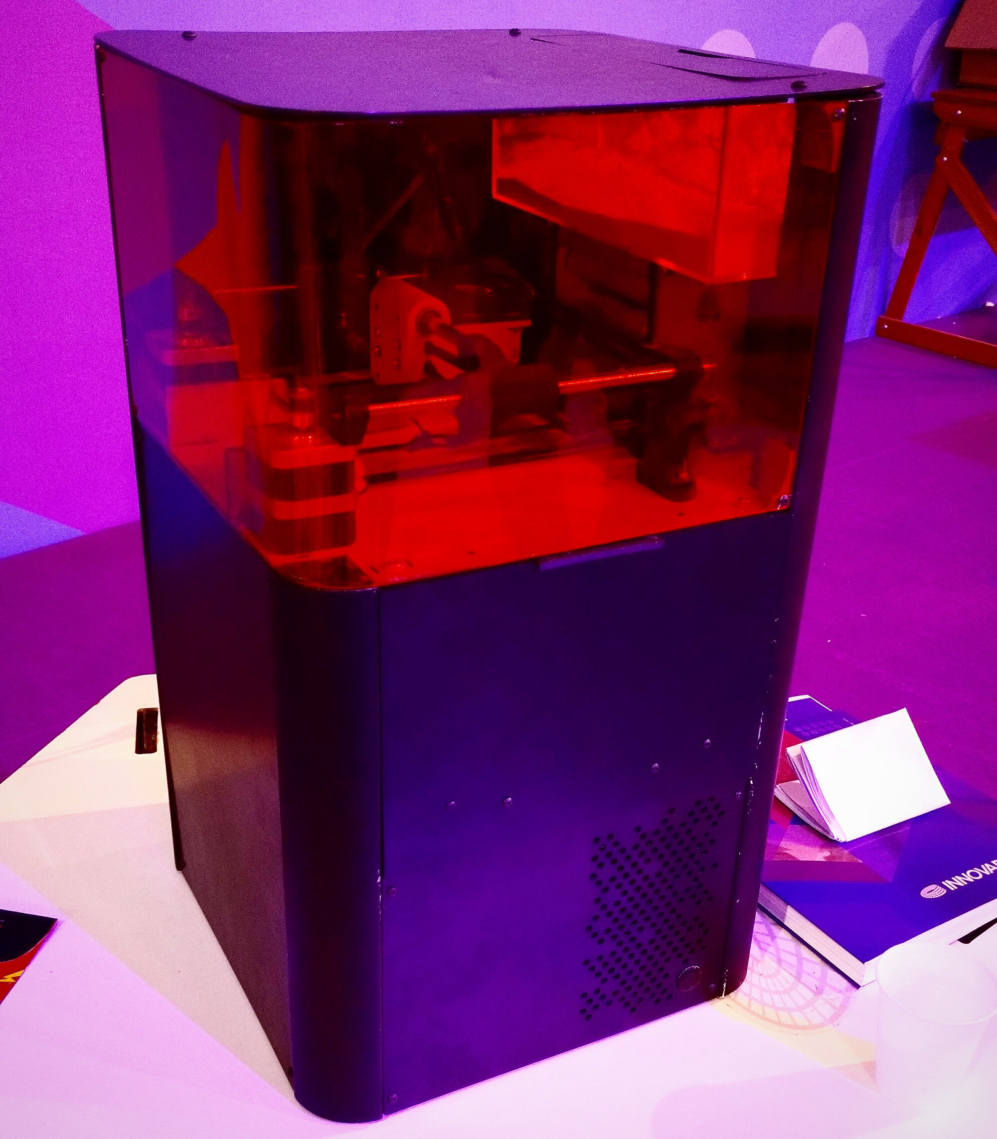 Close-up of the ADI prototype with red-tinted acrylic window revealing the internal sintering mechanism — laser galvanometer module, roller assembly, and powder bed visible inside