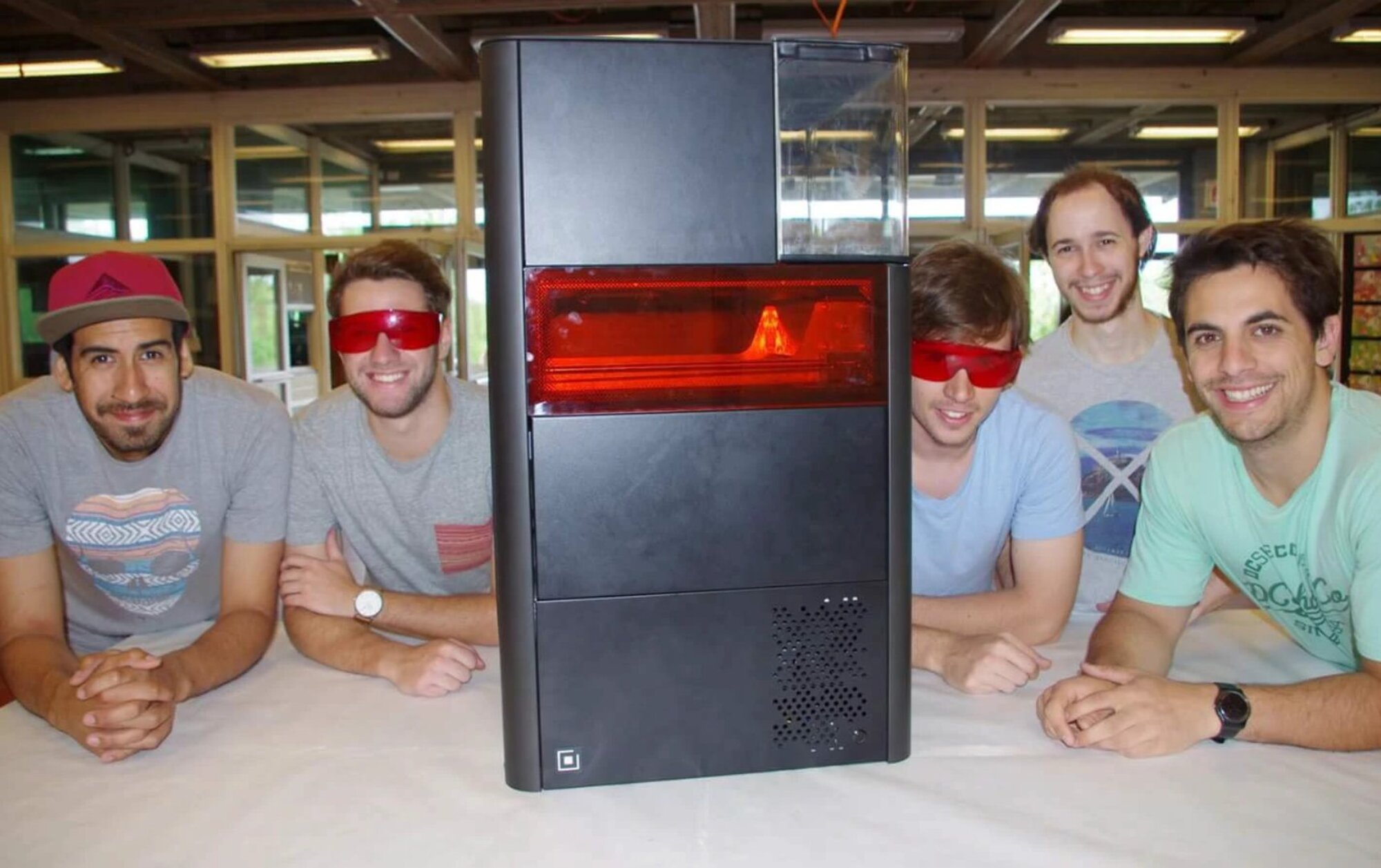The ADI project team — five team members posing with the finished prototype machine on a table, two wearing red safety glasses for the active sintering window